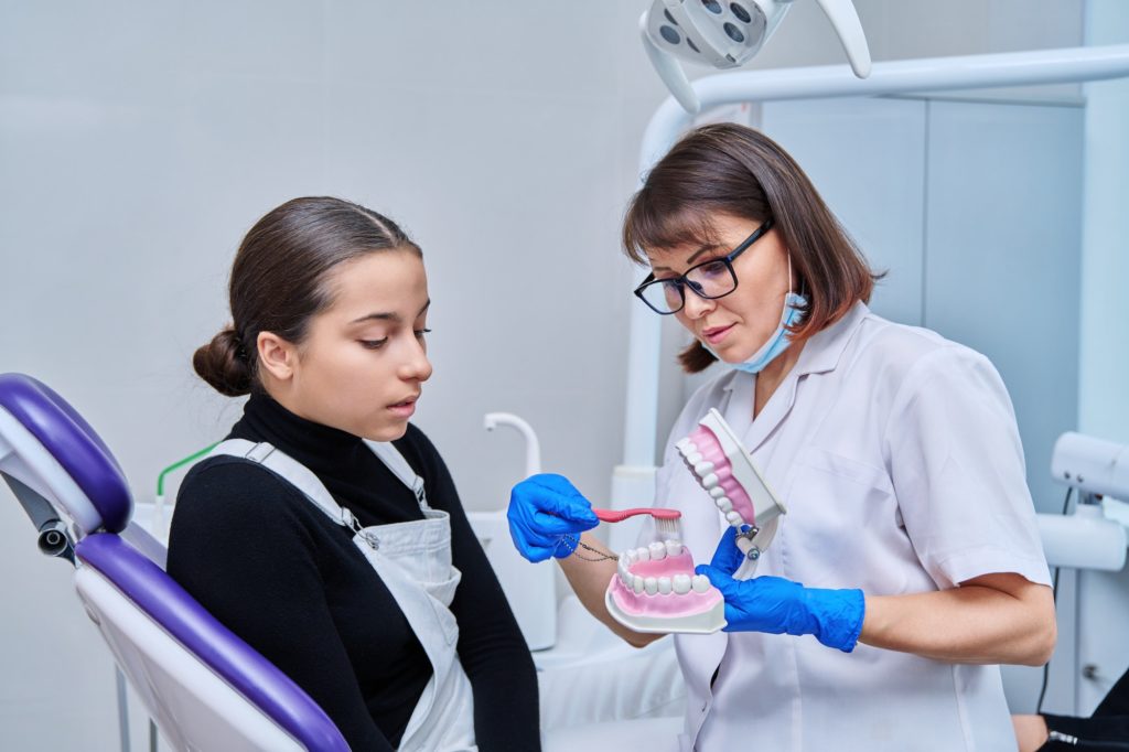 teenage female sitting in dental chair doctor with jaw model and toothbrush مجتبی صیدی دکتر دندان پزشک